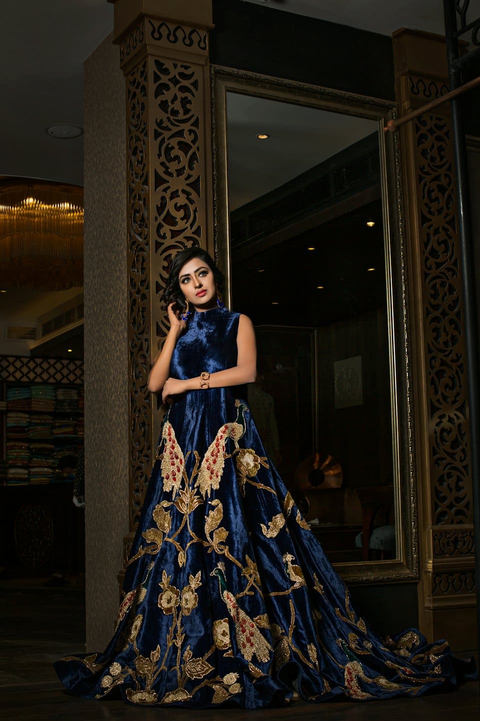 Woman models blue velvet gown with gold embroidery indoors.