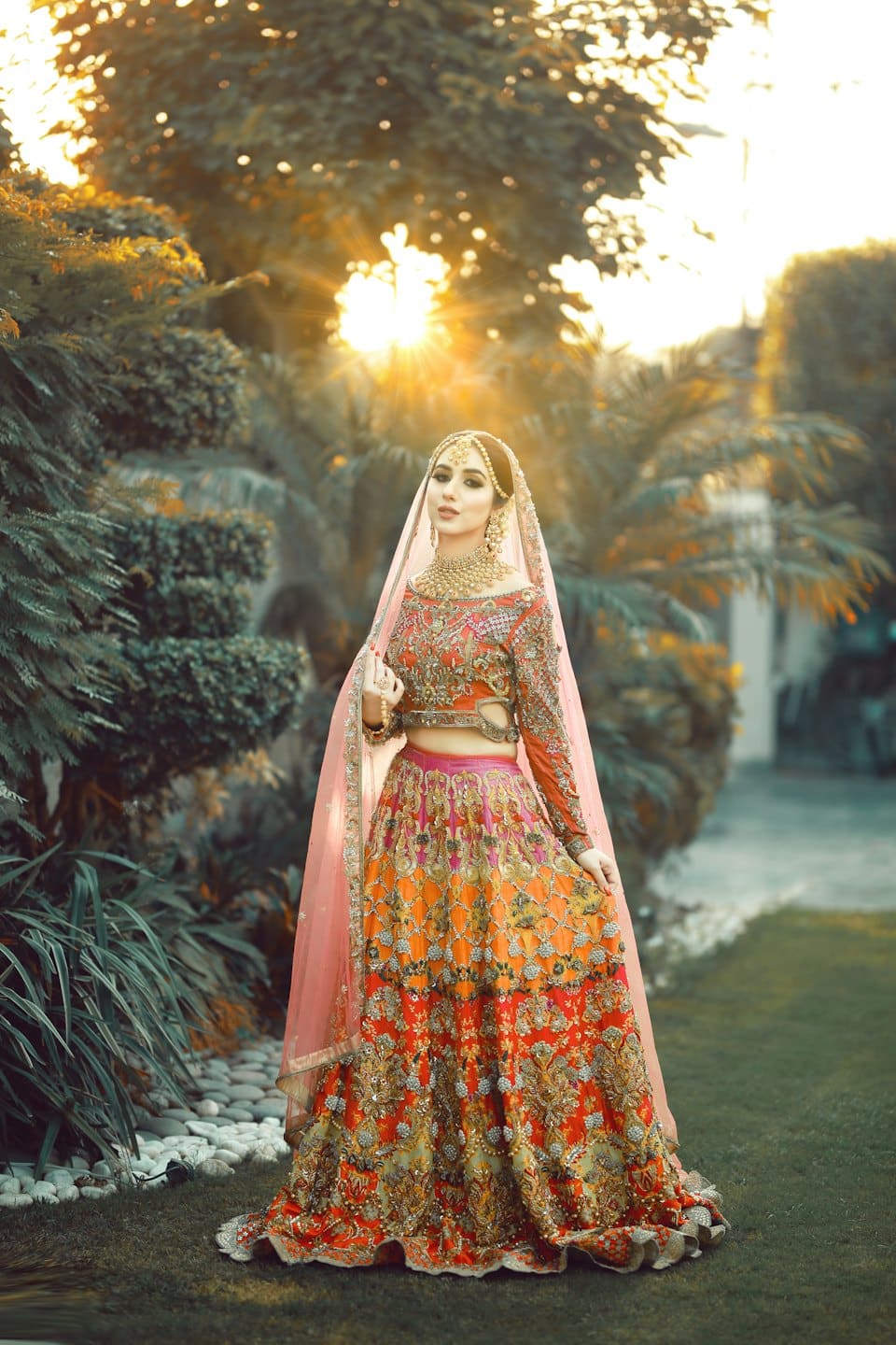 Woman wearing an embroidered lehenga stands in a garden.