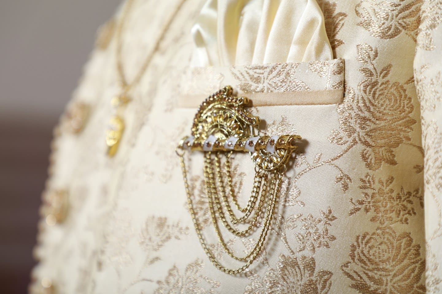 Cream garment with gold embroidery and a decorative brooch.