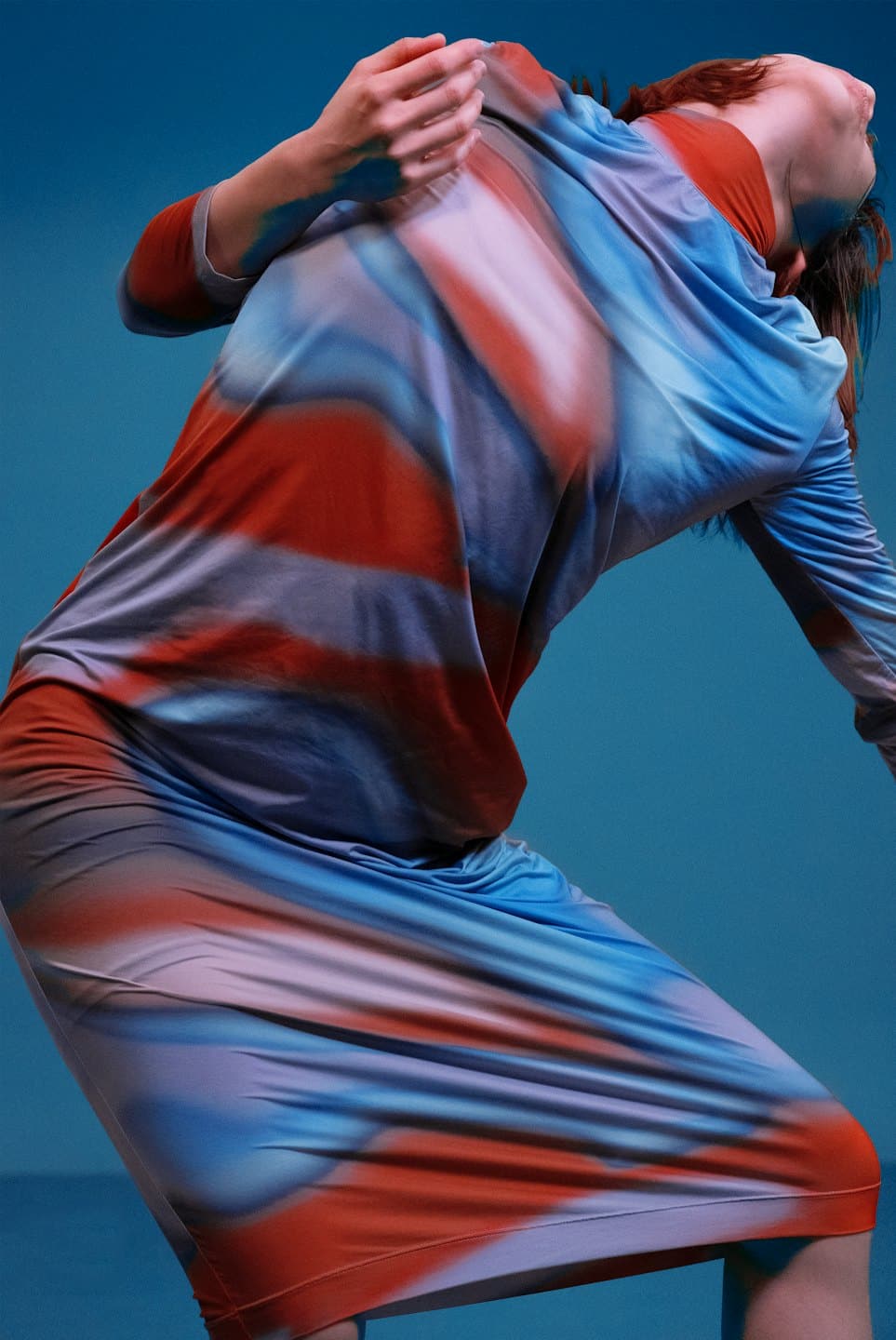 Woman in abstract gradient dress leans back with head tilted up.