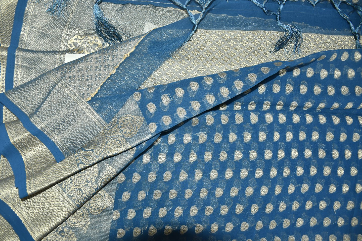 Folded blue fabric with intricate silver and grey embroidered patterns.