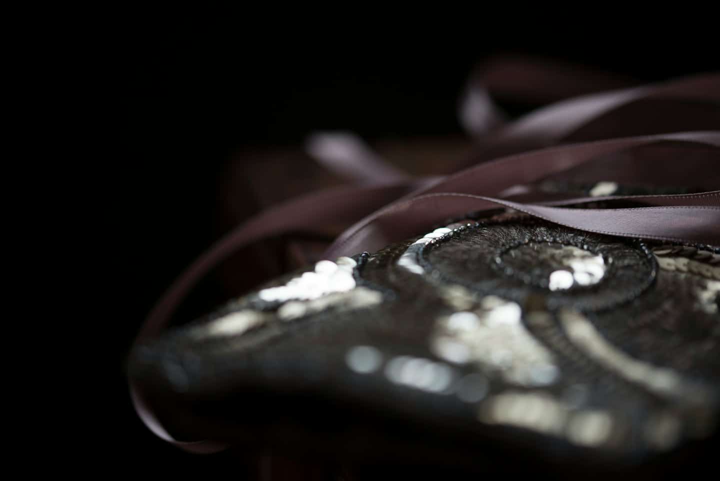 Intricate sequined embroidery and brown ribbon on dark fabric.