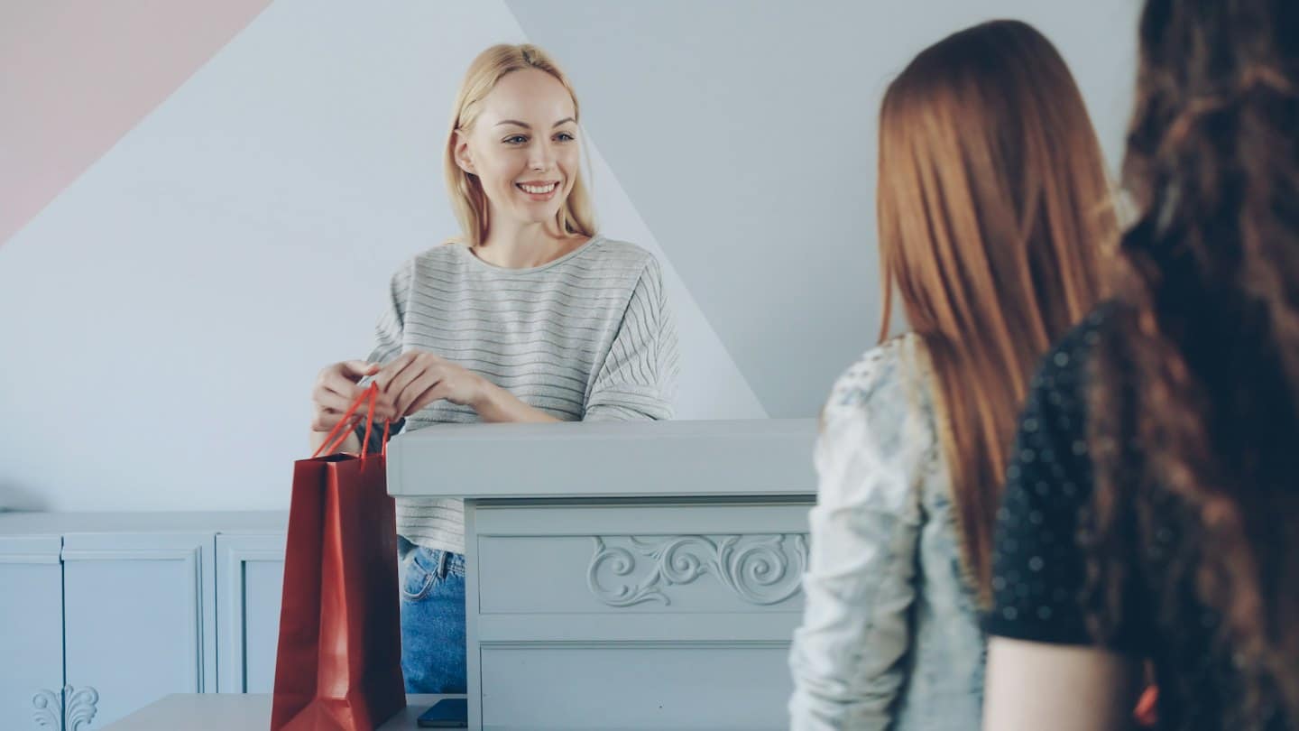 Sales associate smiles and holds shopping bag at counter.